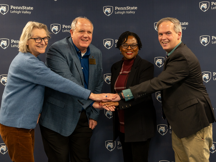 four individuals put their hands in a pile in the middle and smile at the camera 